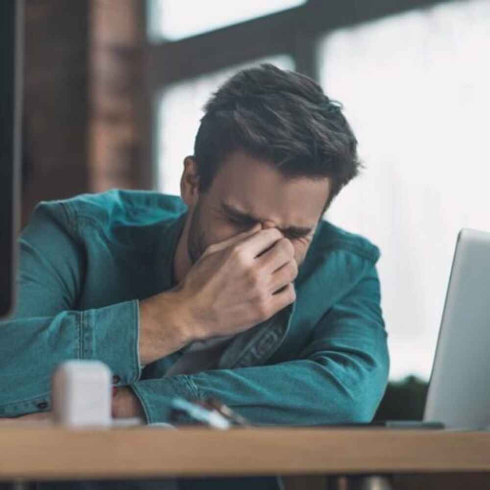 Man holding the top of his nose appearing to experience sinus or nasal issues