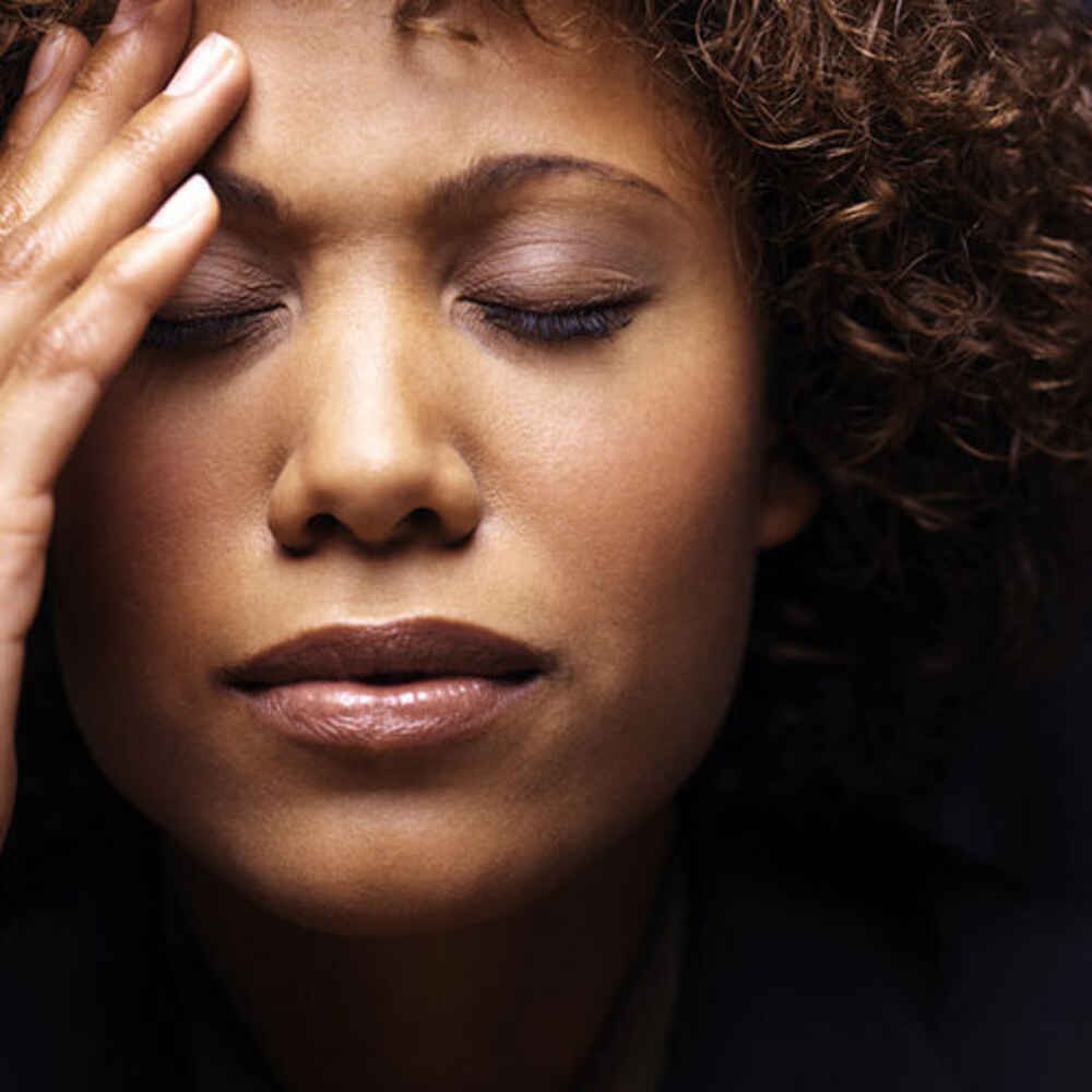 Woman with hand on head appearing to be experiencing a migraine