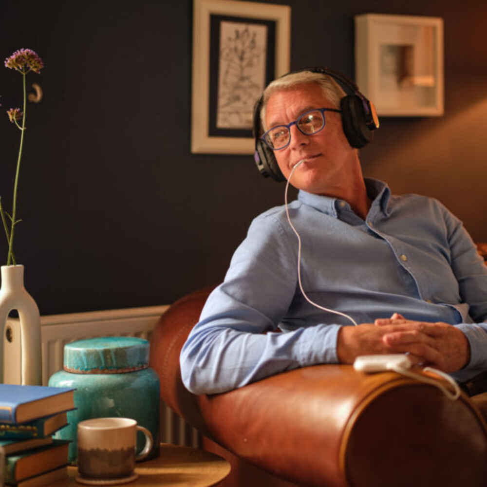 Older man sitting on chair with Lenire Treatment set up to treat his tinnitus